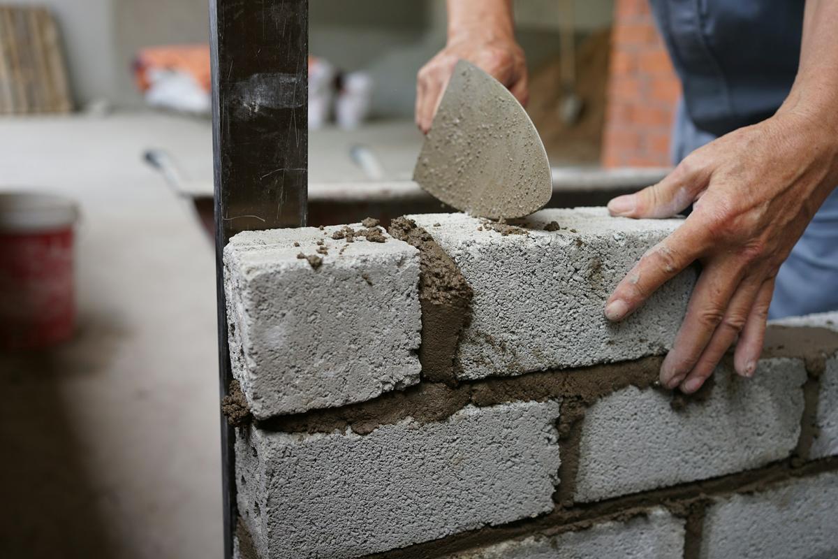 Handen die met een truweel betonblokken metselen