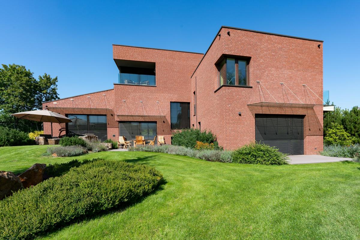 Moderne woning in rode baksteen met een groot gazon, onder een blauwe lucht